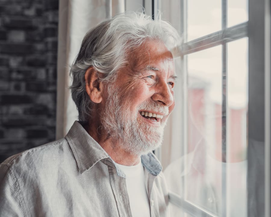 An older man in a collared shirt smiles while looking out the window.
