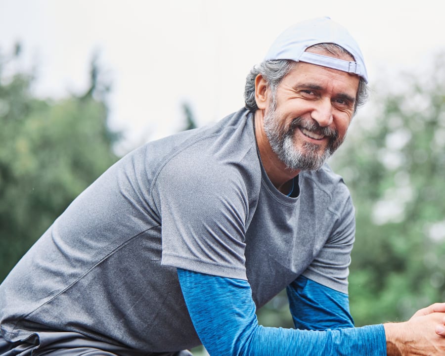 A man sits outside with his ballcap backwards while looking at the camera and smiling.