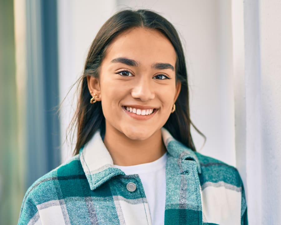 A young woman in a blue plaid shirt is smiling.
