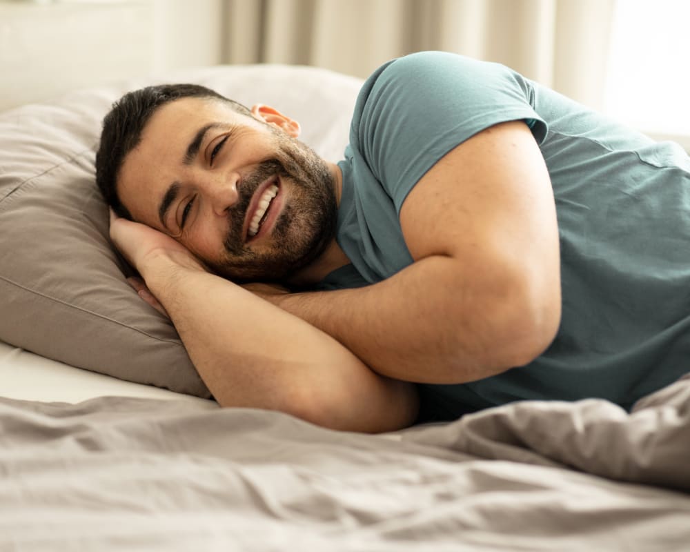 A man lays in bed smiling with his hands under his head.